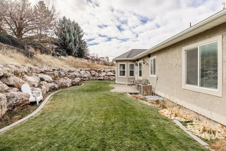 Expansive backyard featuring a manicured lawn, a large stone retaining wall, and a concrete patio