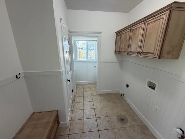 Utility space featuring light wood-finish cabinetry, wainscoting, and tile flooring