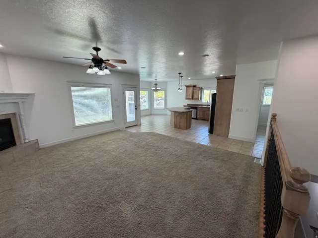 Open-concept living area featuring a fireplace with a decorative mantel, ceiling fan with integrated lighting, and multiple windows
