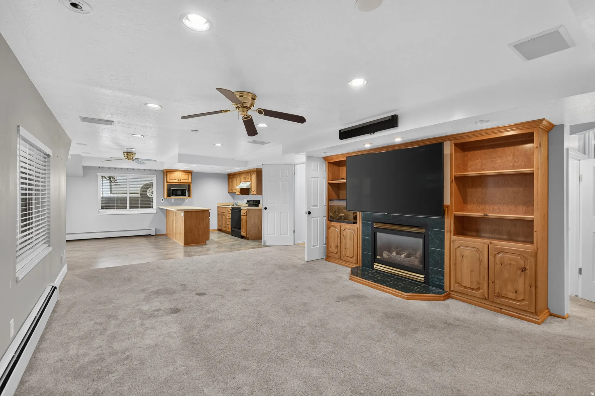 Spacious open-concept room featuring a built-in media center with a fireplace, extensive wood cabinetry, and recessed lighting