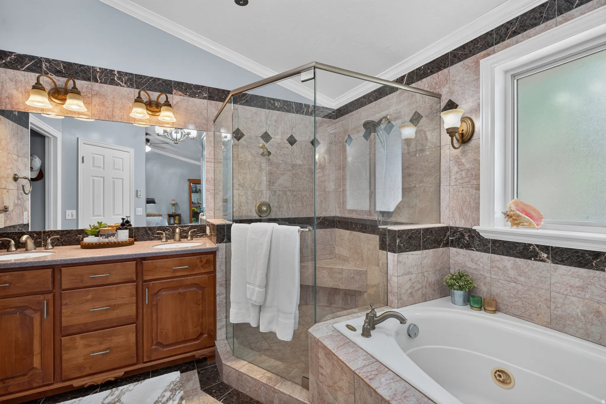 Bathroom featuring a glass-enclosed shower, a built-in jetted tub, a dual-sink vanity with wood cabinetry, and extensive patterned tilework