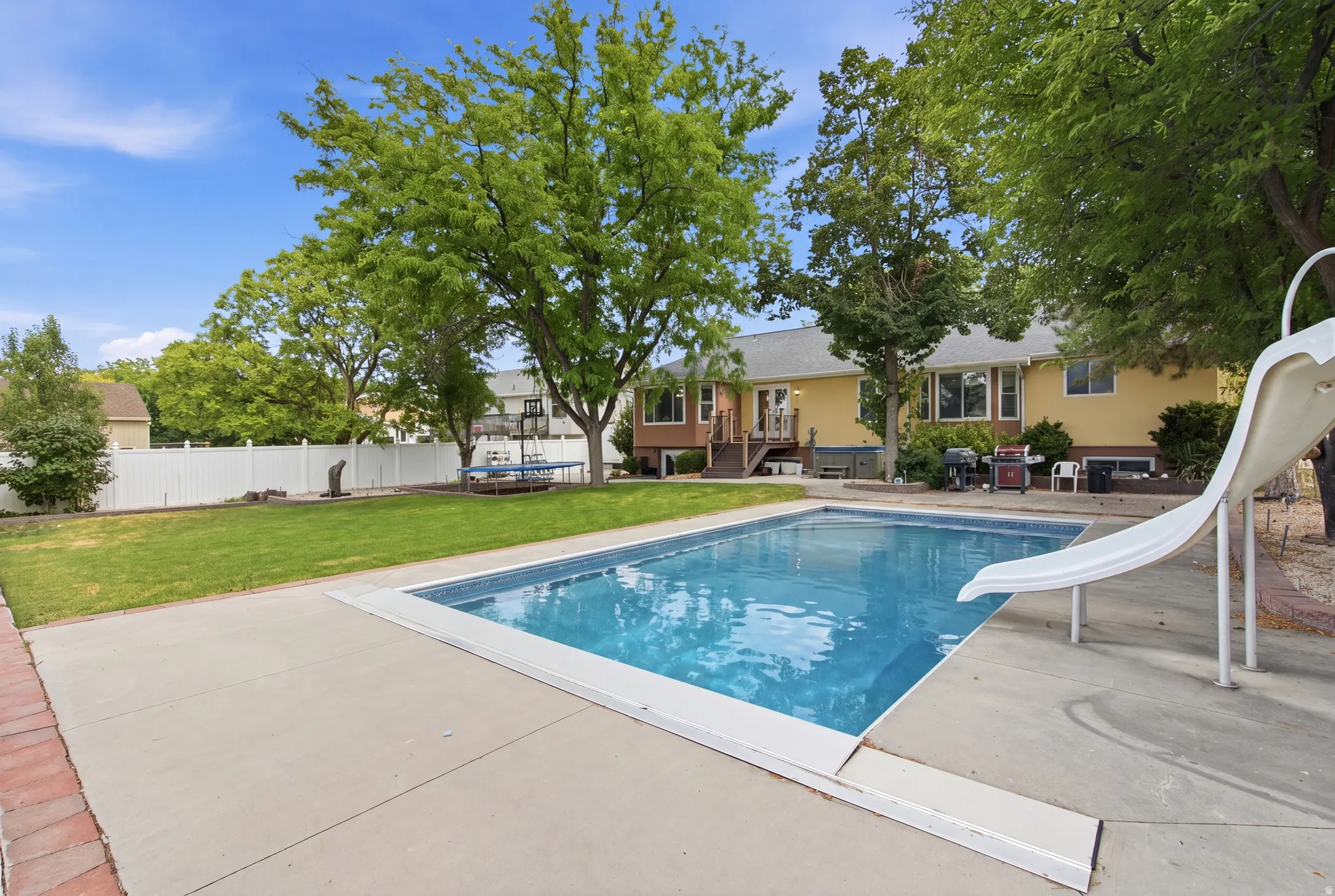 Backyard featuring an inground swimming pool with a slide, extensive concrete patio, and a manicured lawn