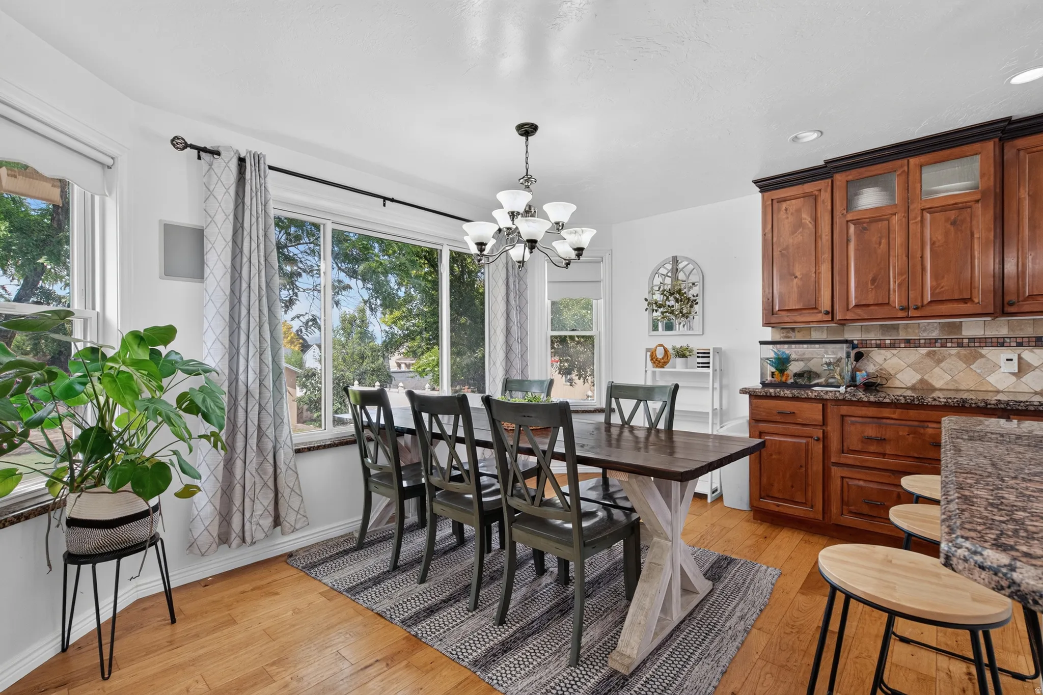 Dining area featuring hardwood flooring, a large picture window, and an adjacent kitchen with wood cabinetry, granite countertops, and a decorative tile backsplash