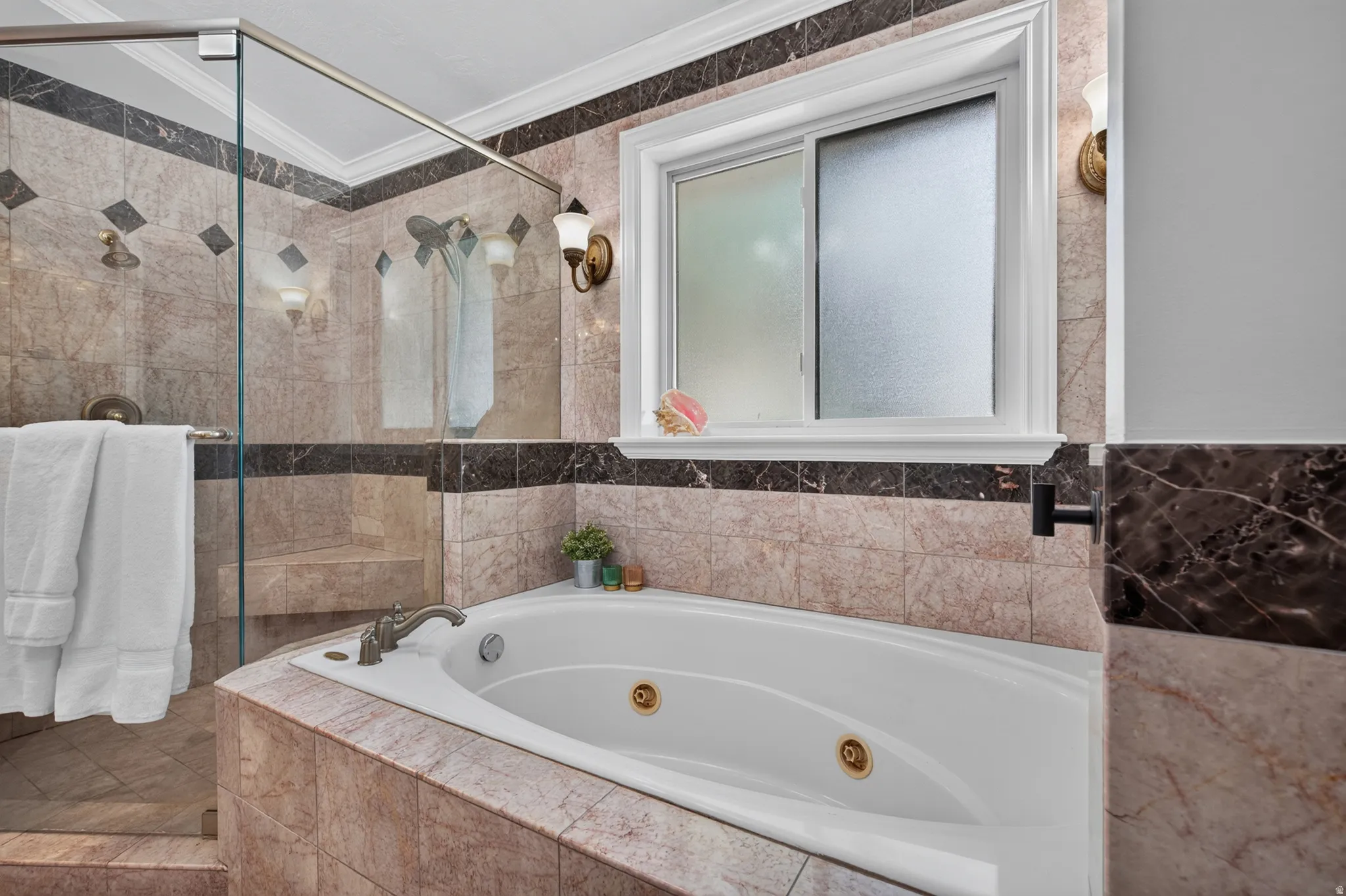 Tiled bathroom featuring a built-in jetted tub, a glass-enclosed shower with a bench, a frosted window, and wall sconces