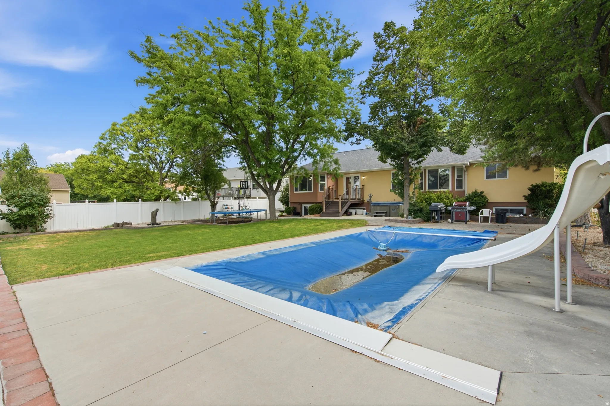 Spacious backyard featuring an in-ground pool with a slide, extensive concrete patio, and a privacy fence