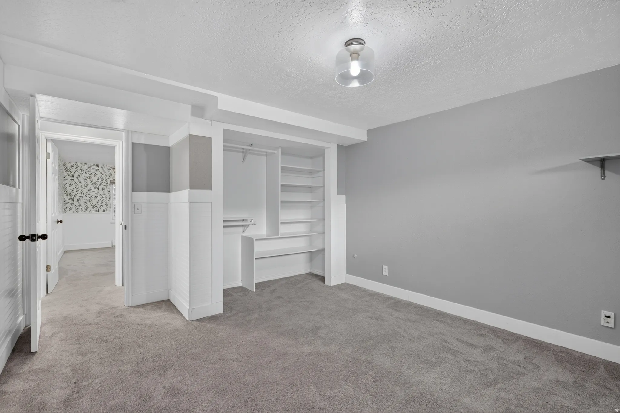 Neutral-toned carpeted room with light gray walls, white baseboards, and a built-in closet system