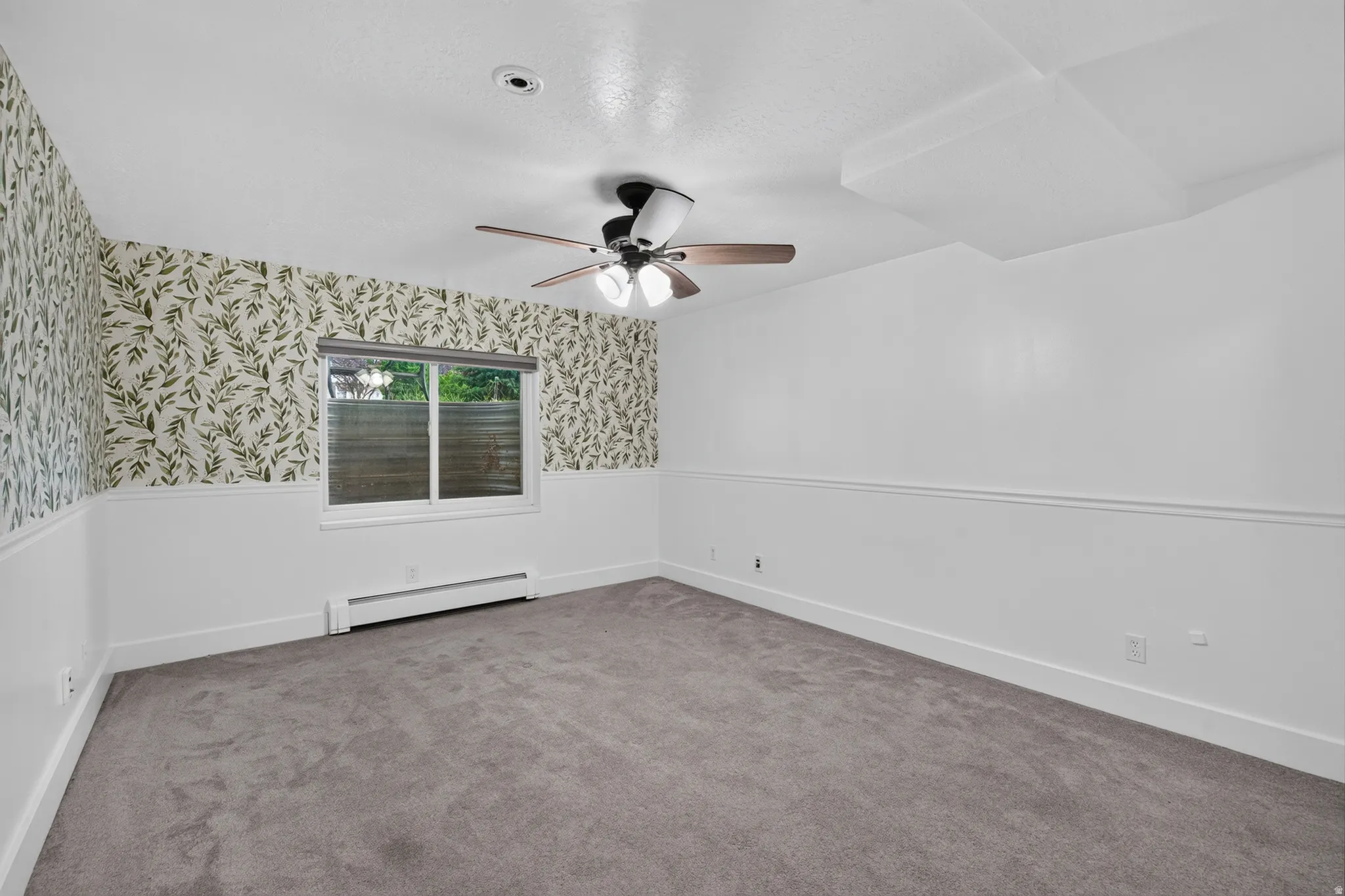 Spacious interior room featuring a large window, leaf-patterned accent wall, and a ceiling fan with integrated lighting