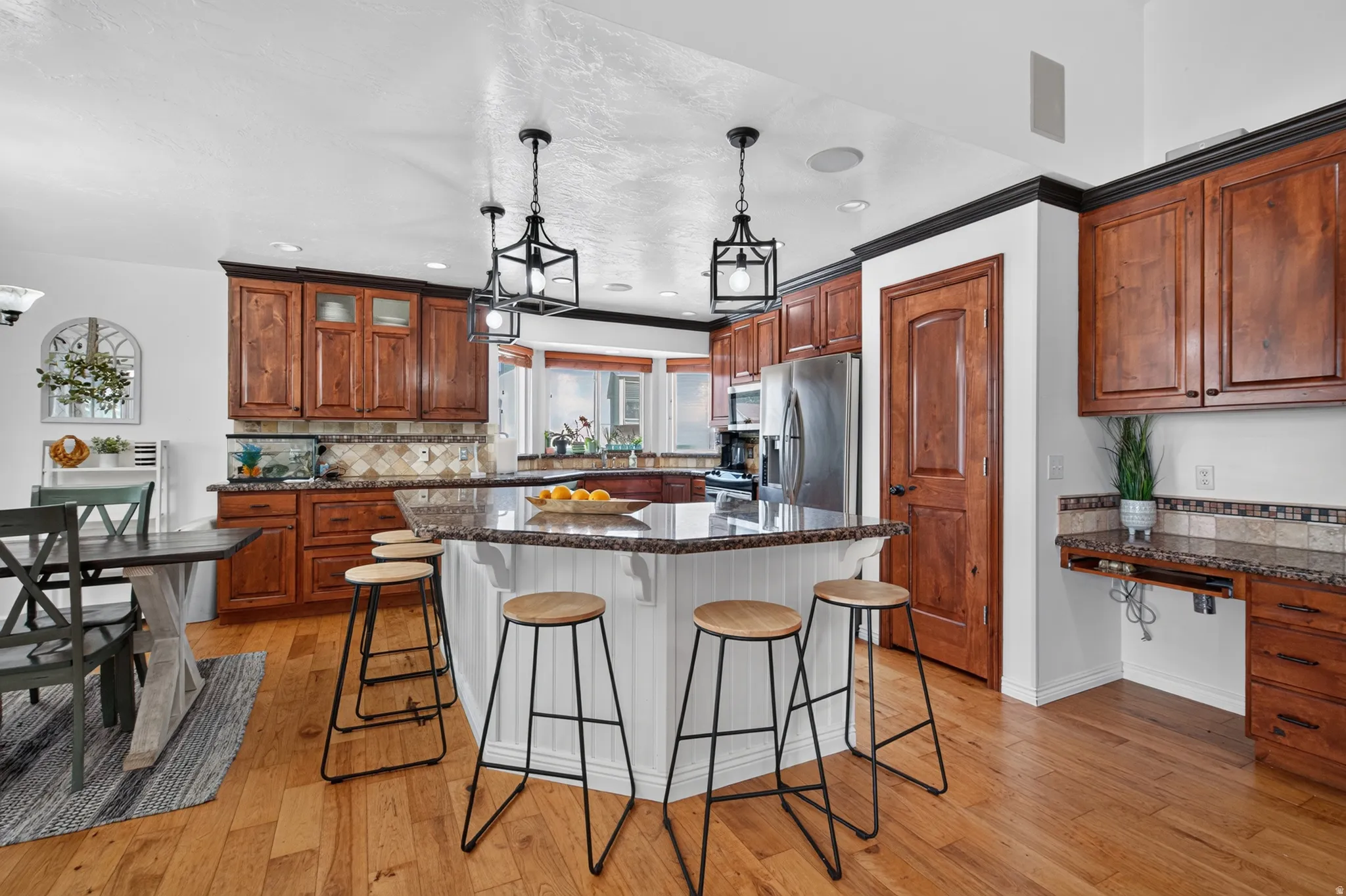 Kitchen featuring an extended island with seating, wood-finish flooring, recessed lighting, stainless steel appliances, and a built-in desk area