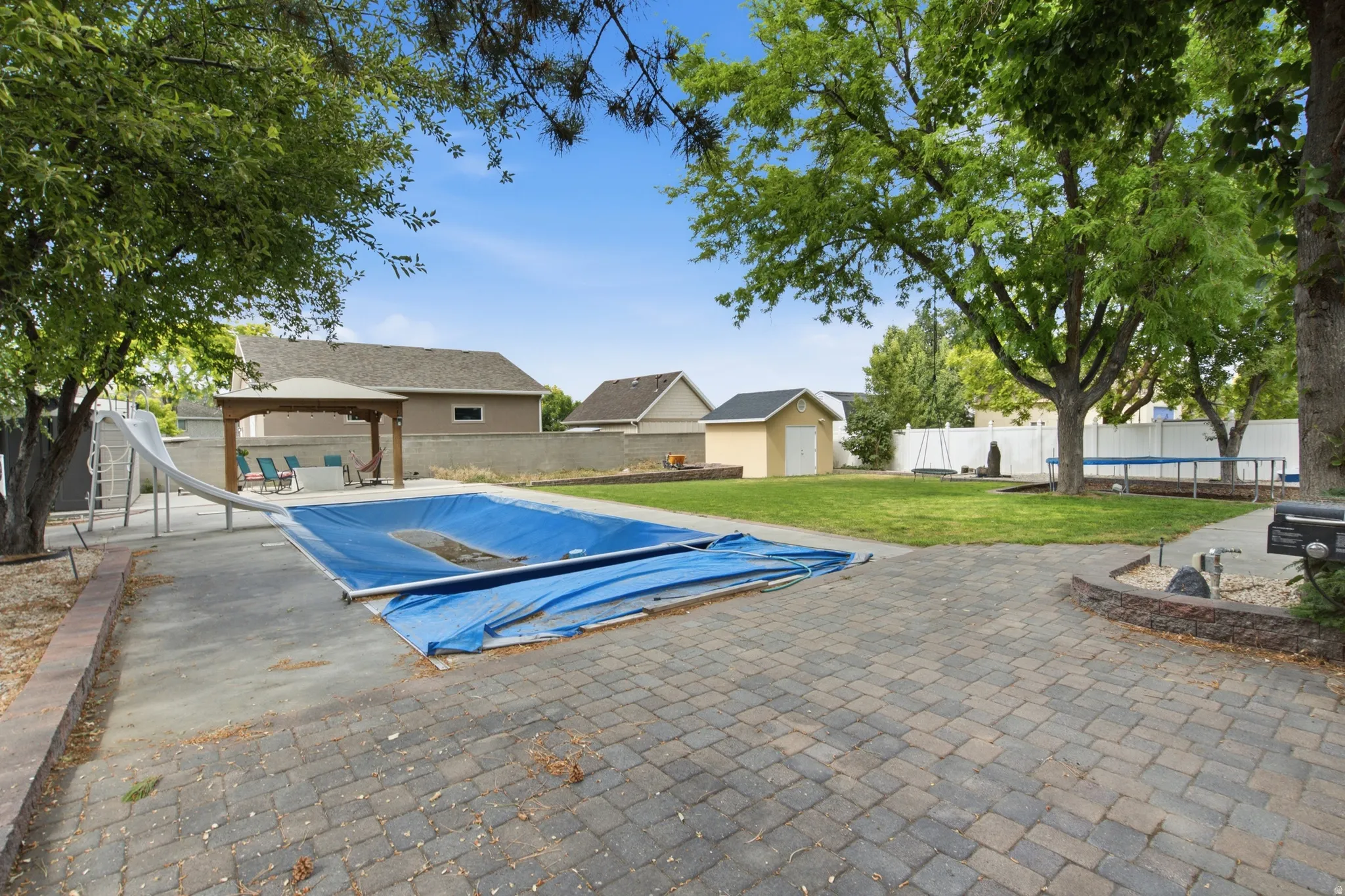 Expansive backyard featuring a covered swimming pool with a waterslide, a wooden gazebo, a paved patio area, and a large grassy lawn