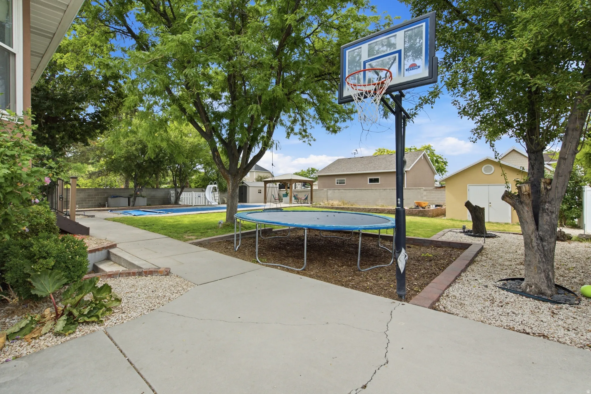 Expansive rear yard featuring mature trees, a concrete pathway, a swimming pool, and a detached shed