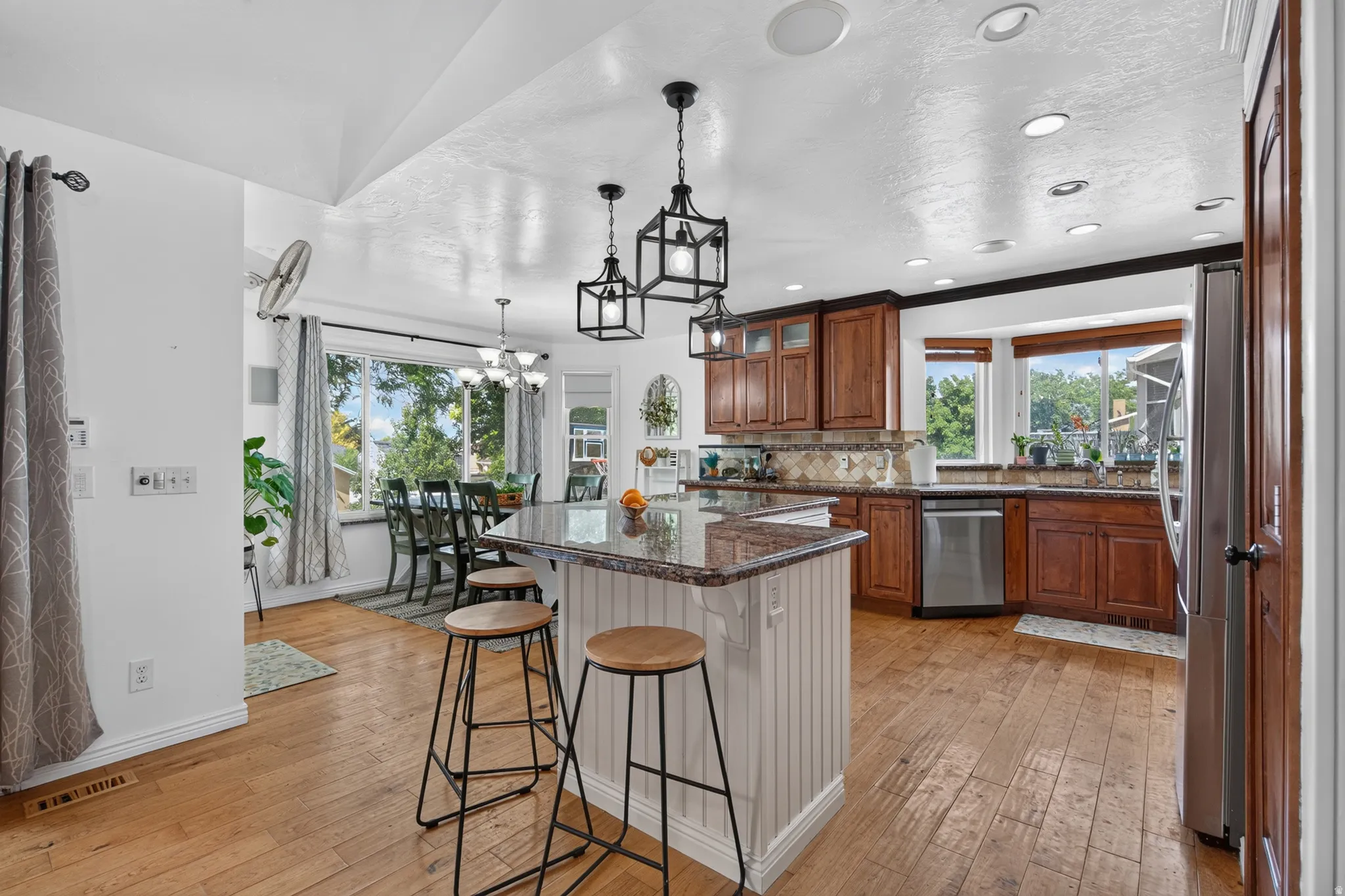 Spacious kitchen featuring wood-finish flooring, recessed lighting, a central island with a granite-style countertop, built-in wood cabinetry, and stainless steel appliances