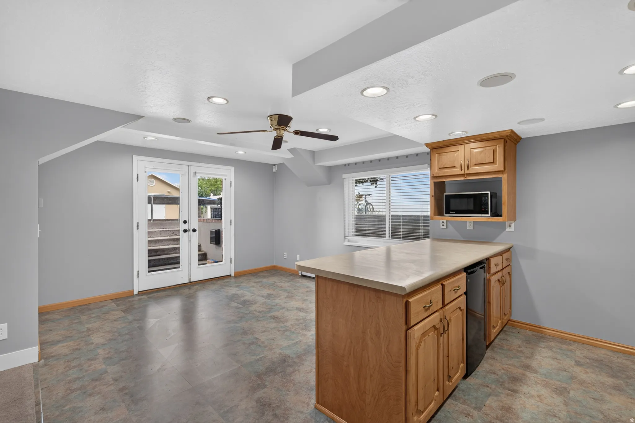 Recessed lighting illuminates this room featuring French doors, a ceiling fan, and a built-in wood-finish island with integrated cabinetry and a beverage refrigerator