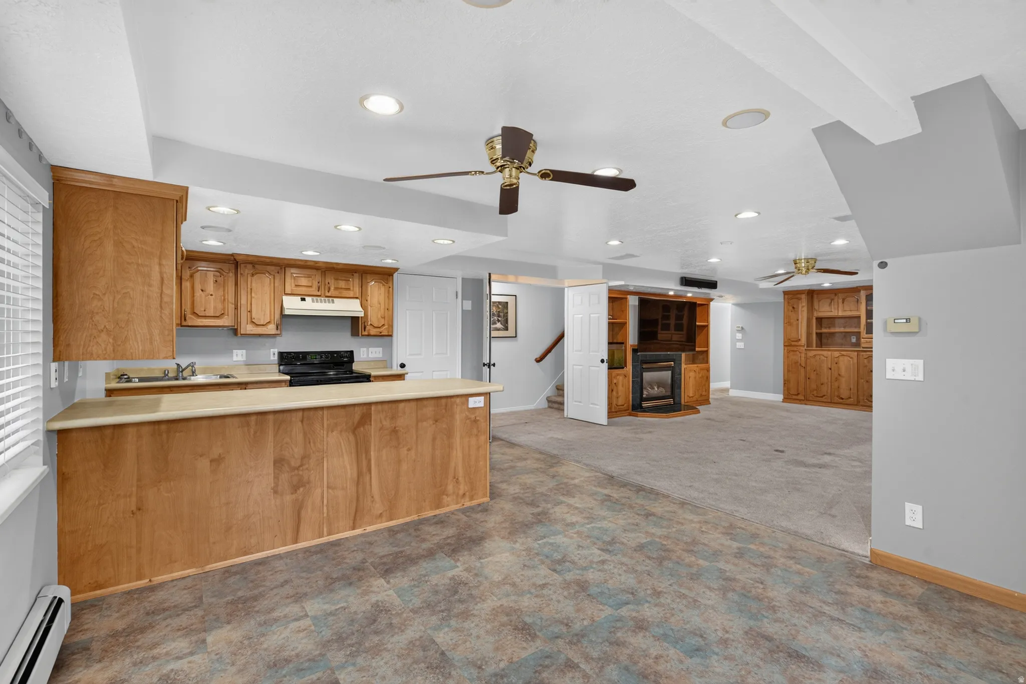 Spacious lower level featuring a full kitchen with wood cabinetry, a built-in entertainment center with a fireplace, recessed lighting, and ceiling fans
