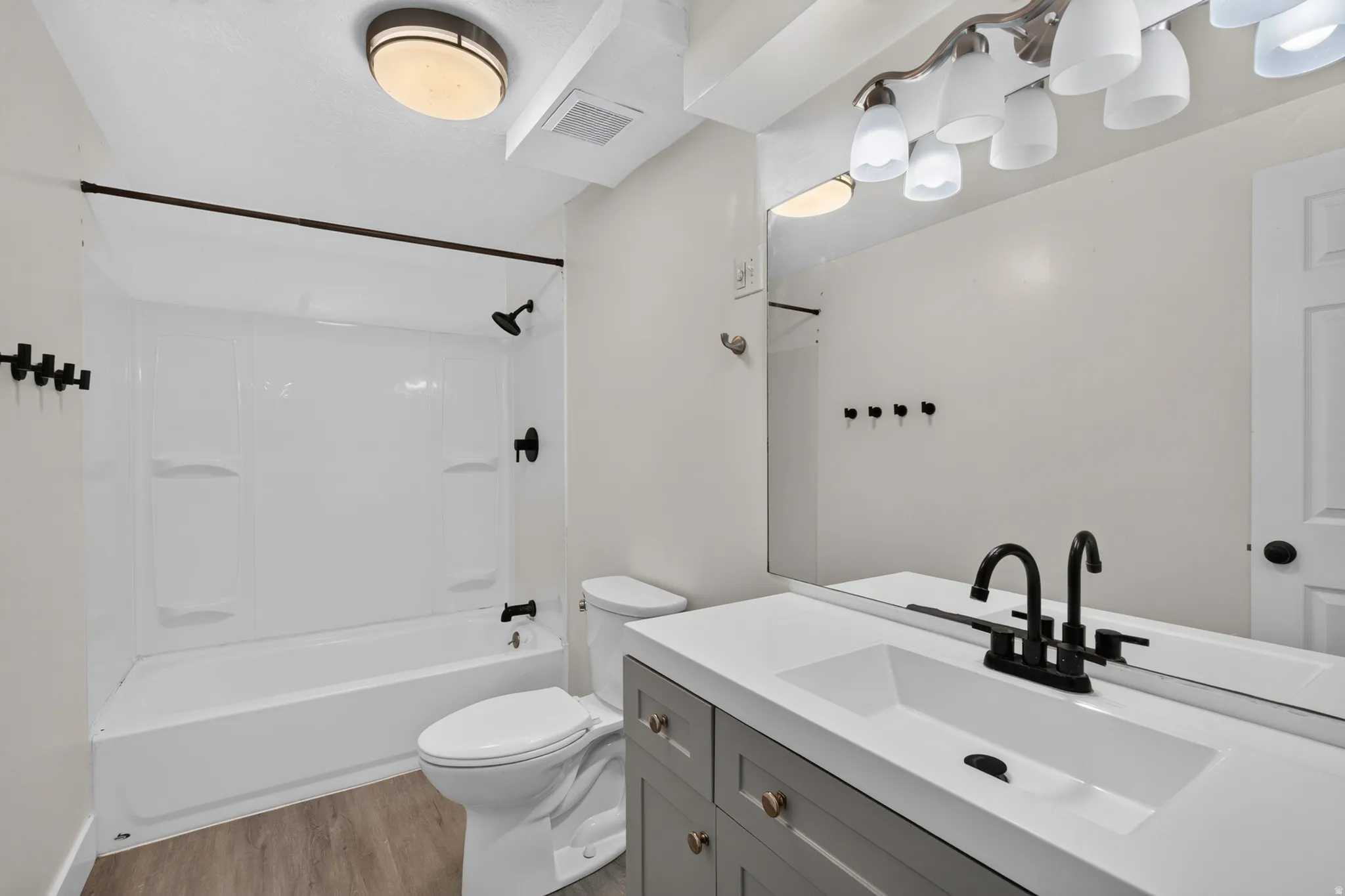 Bathroom featuring a white bathtub and shower surround, a vanity with a white countertop and integrated sink, a large wall-mounted mirror, and wood-finish flooring