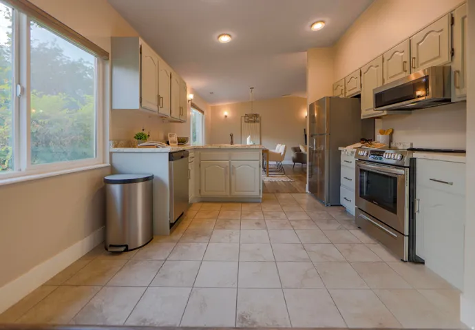 Kitchen featuring tile flooring, painted cabinetry, light countertops, stainless steel appliances, and an island with additional storage