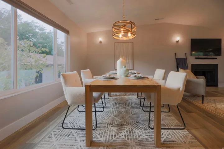 Vaulted ceilings with a circular gold-finish chandelier, large picture window, wood-finish flooring, and a fireplace with a mantel