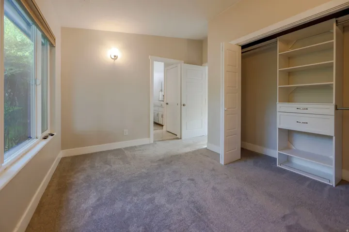 Plush gray carpeting, built-in closet organization system, sconce lighting, and a window with a wood-finish blind