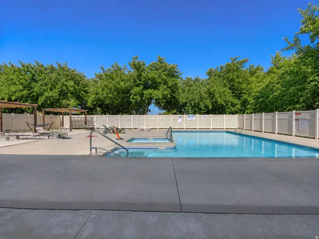 Outdoor swimming pool with an integrated spa, surrounded by a concrete deck and a white privacy fence
