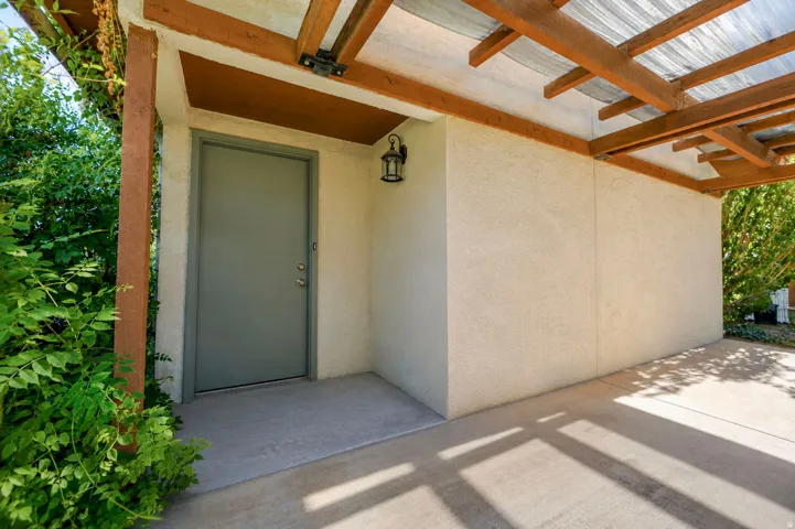 Covered entryway with concrete flooring, stucco wall finish, and a wood-beamed overhang with a translucent roof