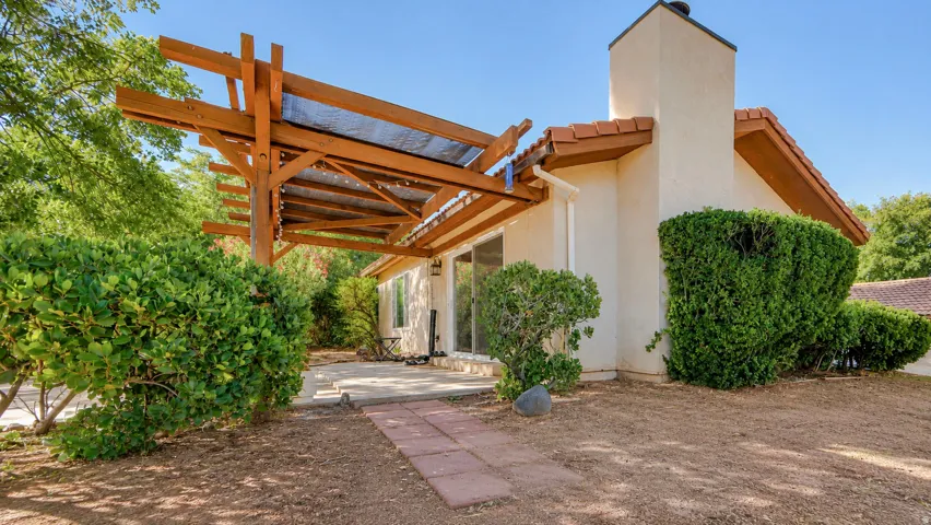 Exterior patio with a wood pergola, tile roof accents, stucco siding, and mature landscaping