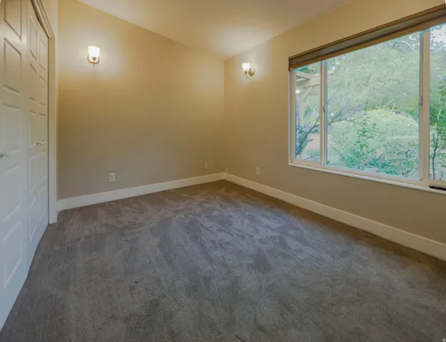 Neutral-toned walls, gray carpeting, dual sconce lighting, and a large window with a scenic outdoor backdrop