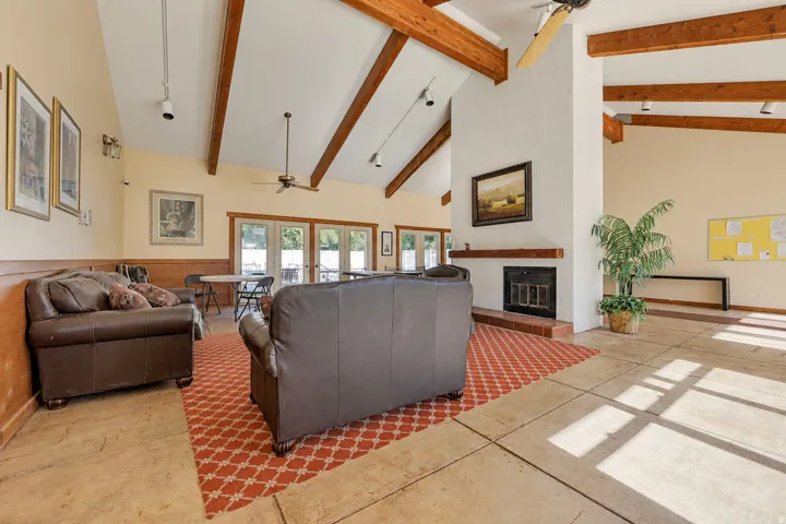 Vaulted ceilings with exposed wood beams, a prominent fireplace with a wood mantel, light-toned flooring, and glass-paned doors