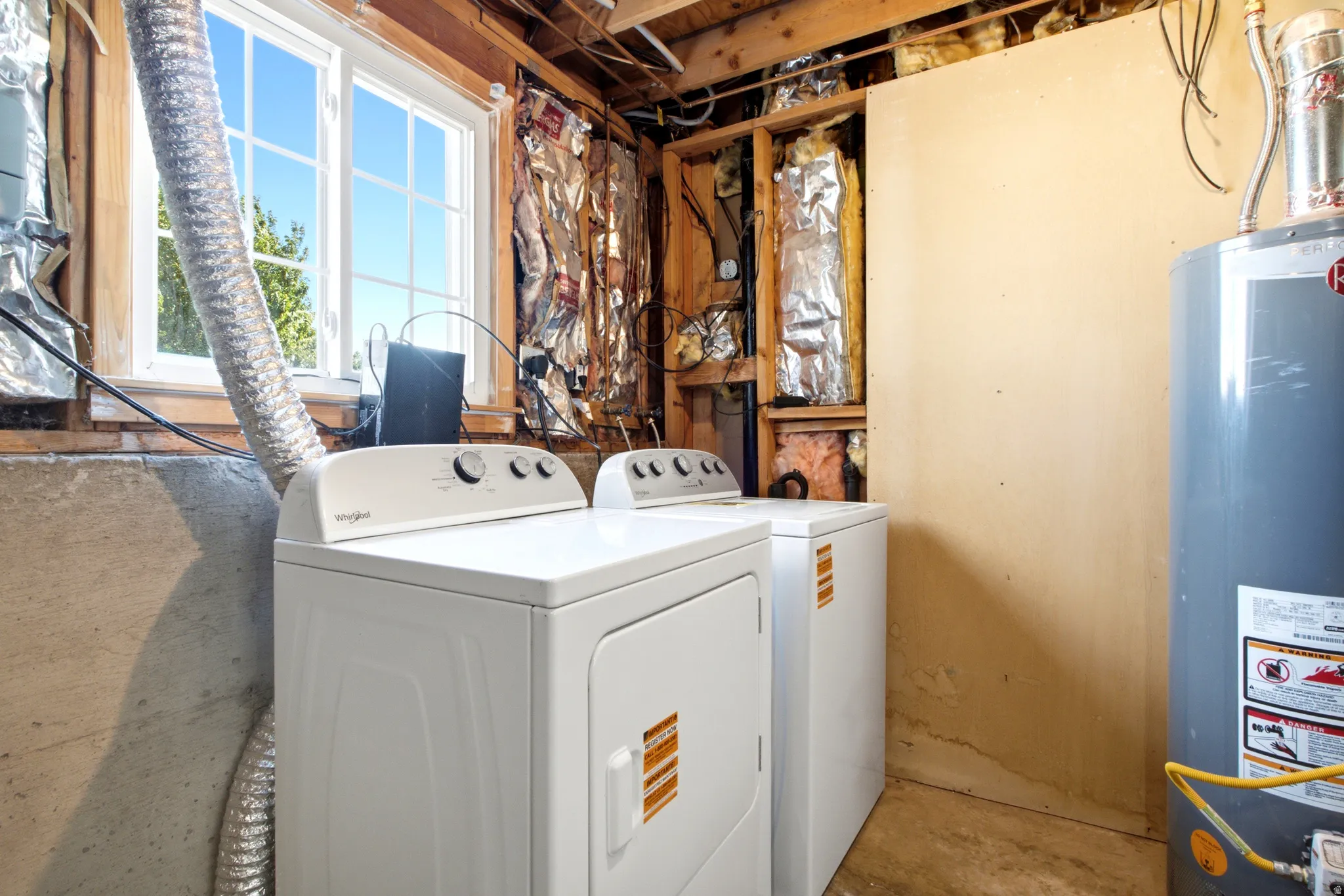 Laundry area featuring a window, exposed wood framing, concrete foundation, and a hot water heater
