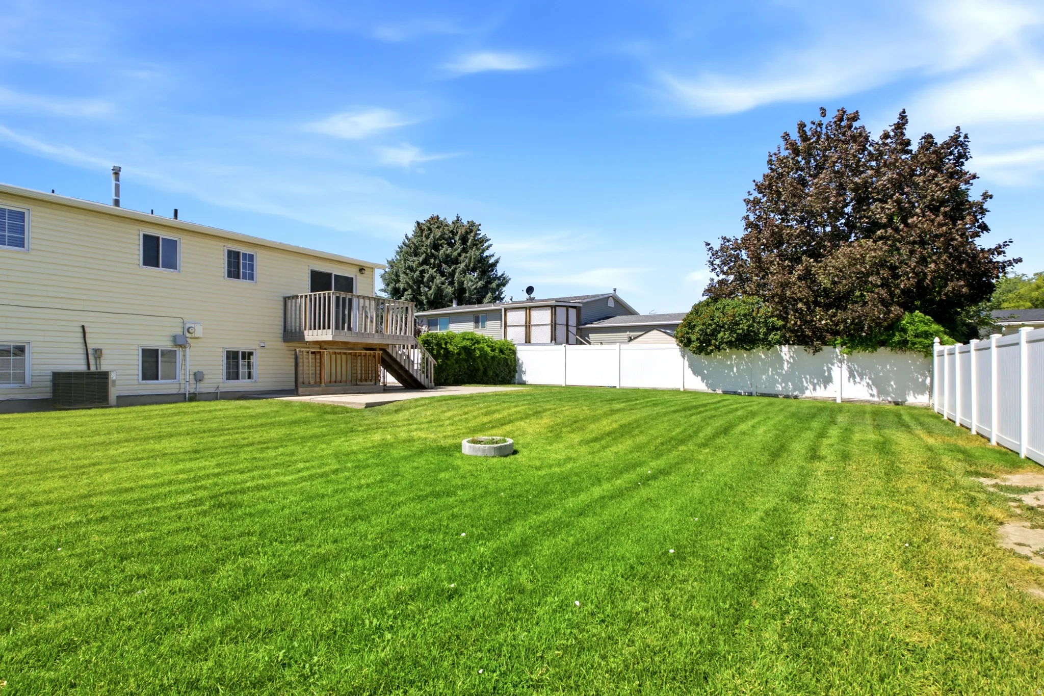 Expansive lawn with a white vinyl fence, offering a wood deck and concrete patio at the rear of the residence