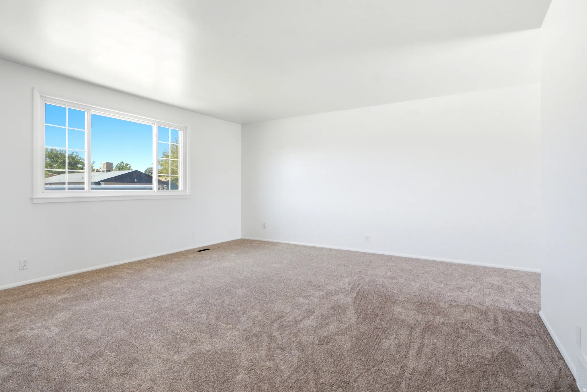 Spacious interior room featuring light brown carpeting and crisp white walls