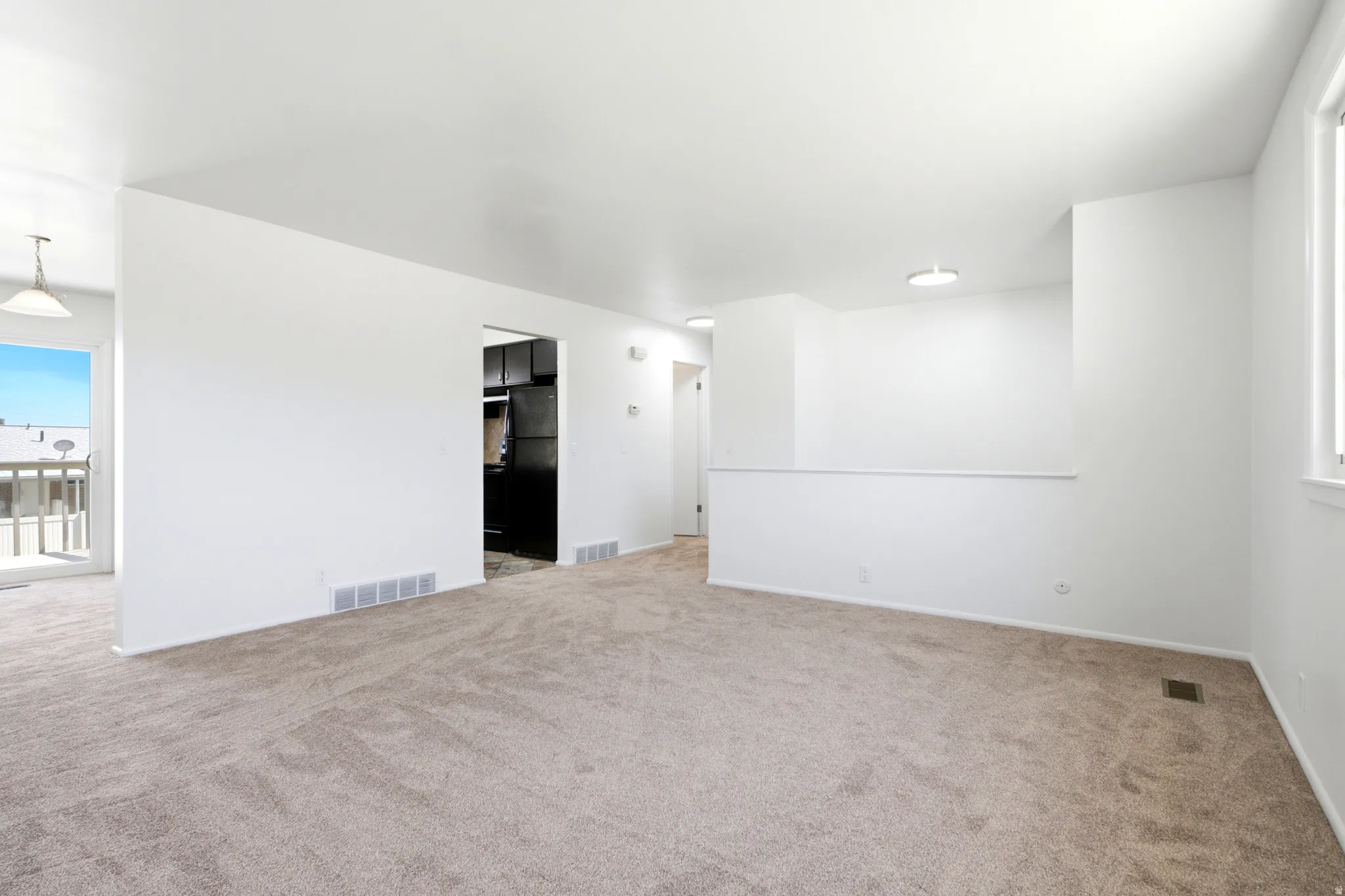 Spacious living area featuring neutral carpeting, white walls, and a large window providing natural light