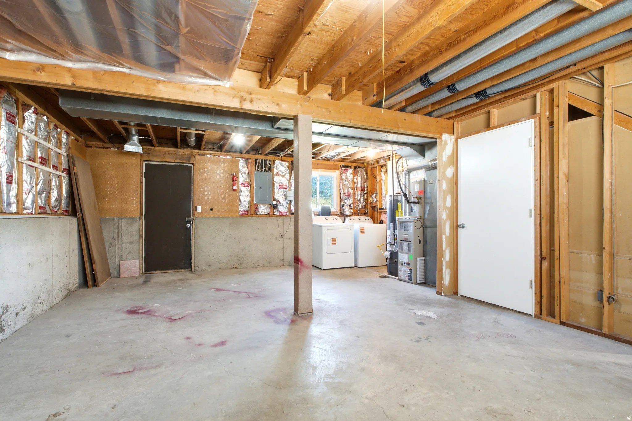 Unfinished basement featuring exposed wood beams, concrete flooring, and partial wall insulation