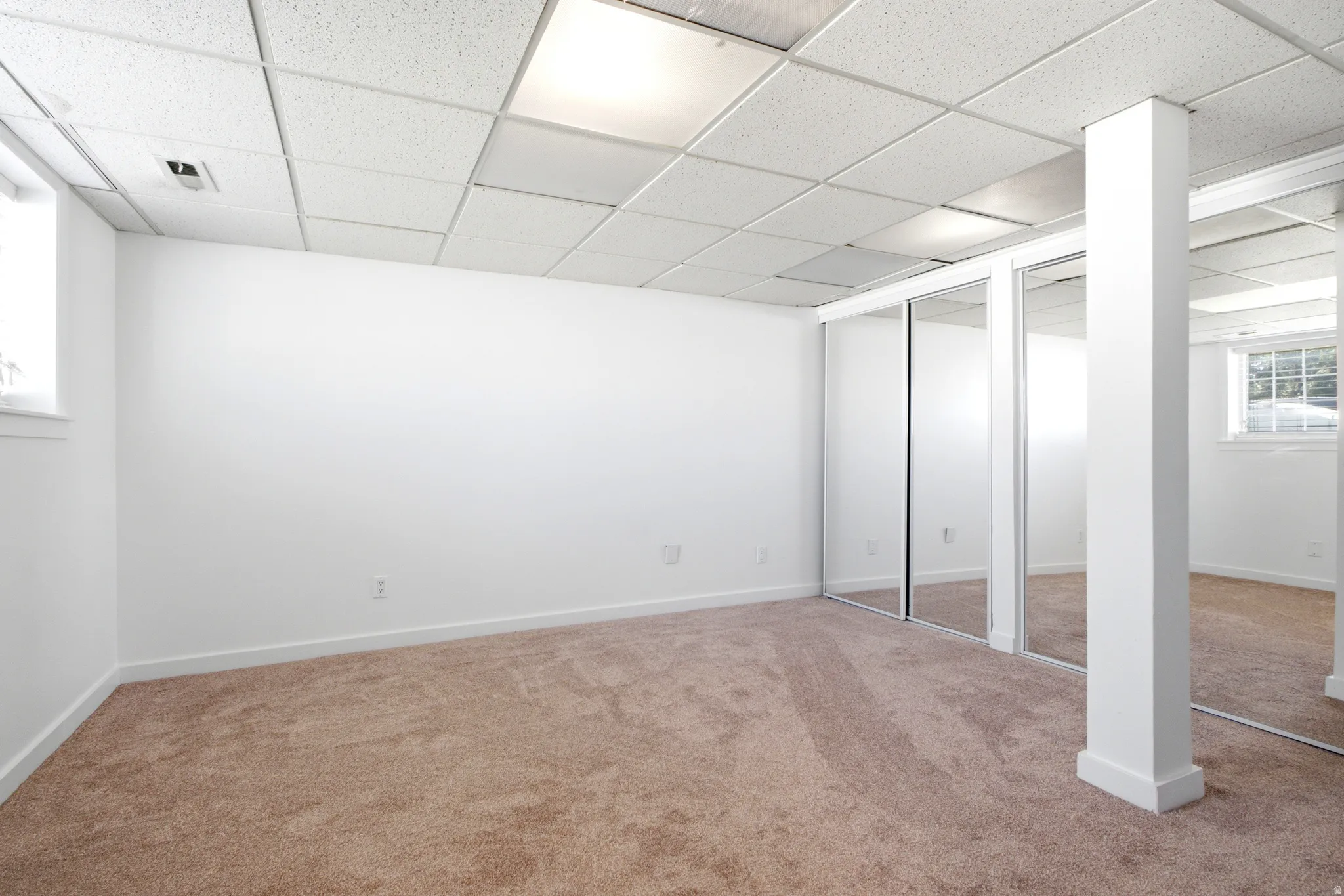 Spacious room featuring neutral carpeting, white walls, and a drop ceiling with integrated lighting