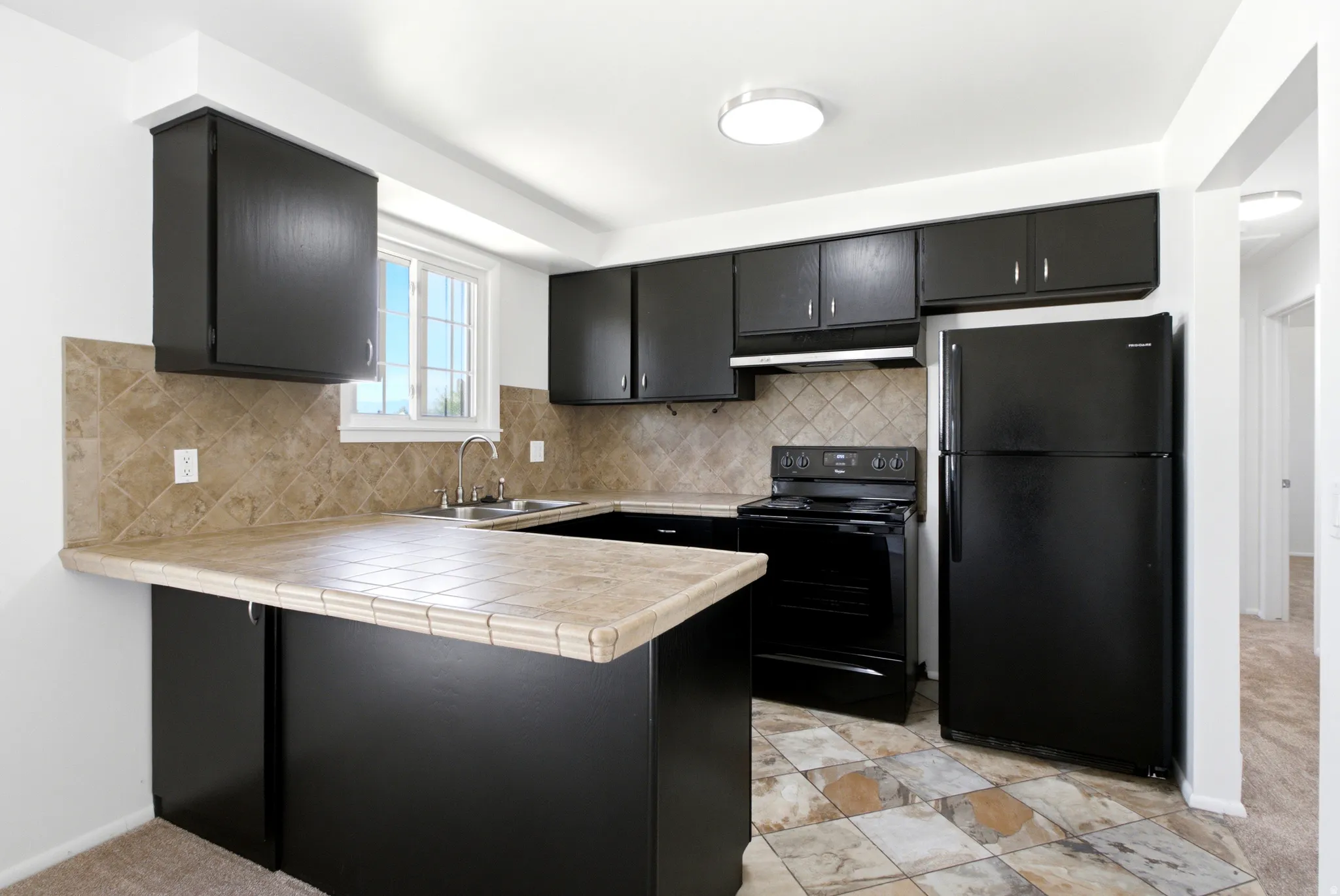 Kitchen featuring dark cabinetry, ceramic tile countertops, stainless steel sink, black electric range, and black refrigerator