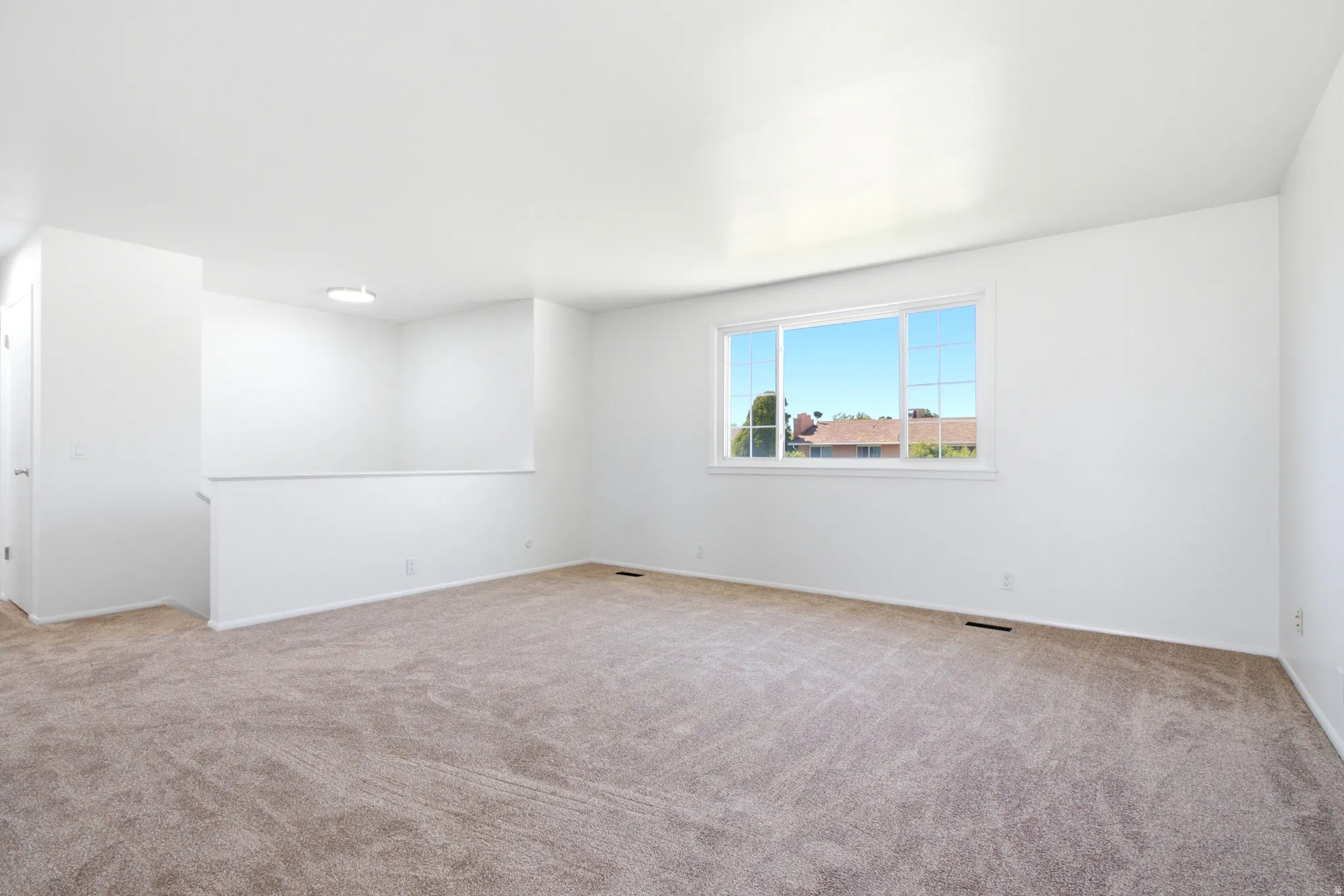 Spacious interior featuring a large window, neutral carpeting, white painted walls, and a recessed lighting fixture