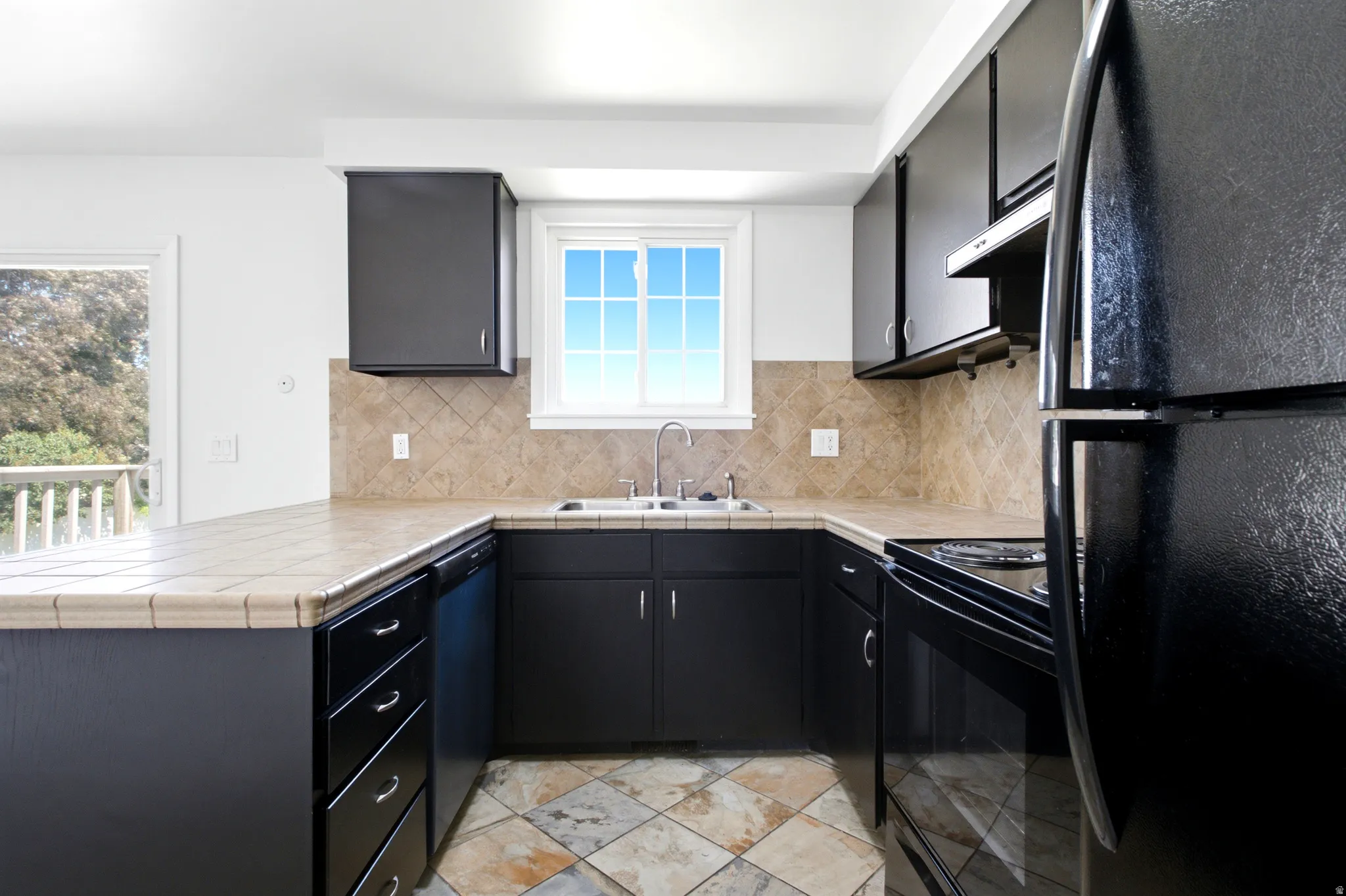U-shaped kitchen featuring black cabinetry, tile countertops, a tile backsplash, and black appliances