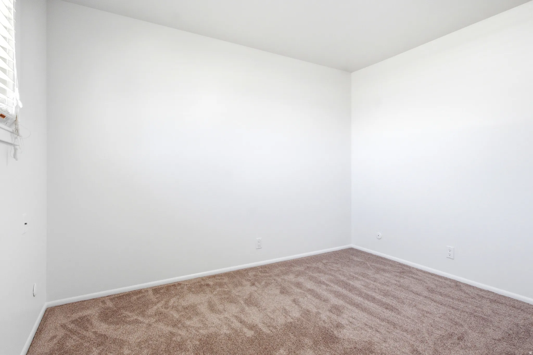 Carpeted interior room featuring white walls and a window with blinds
