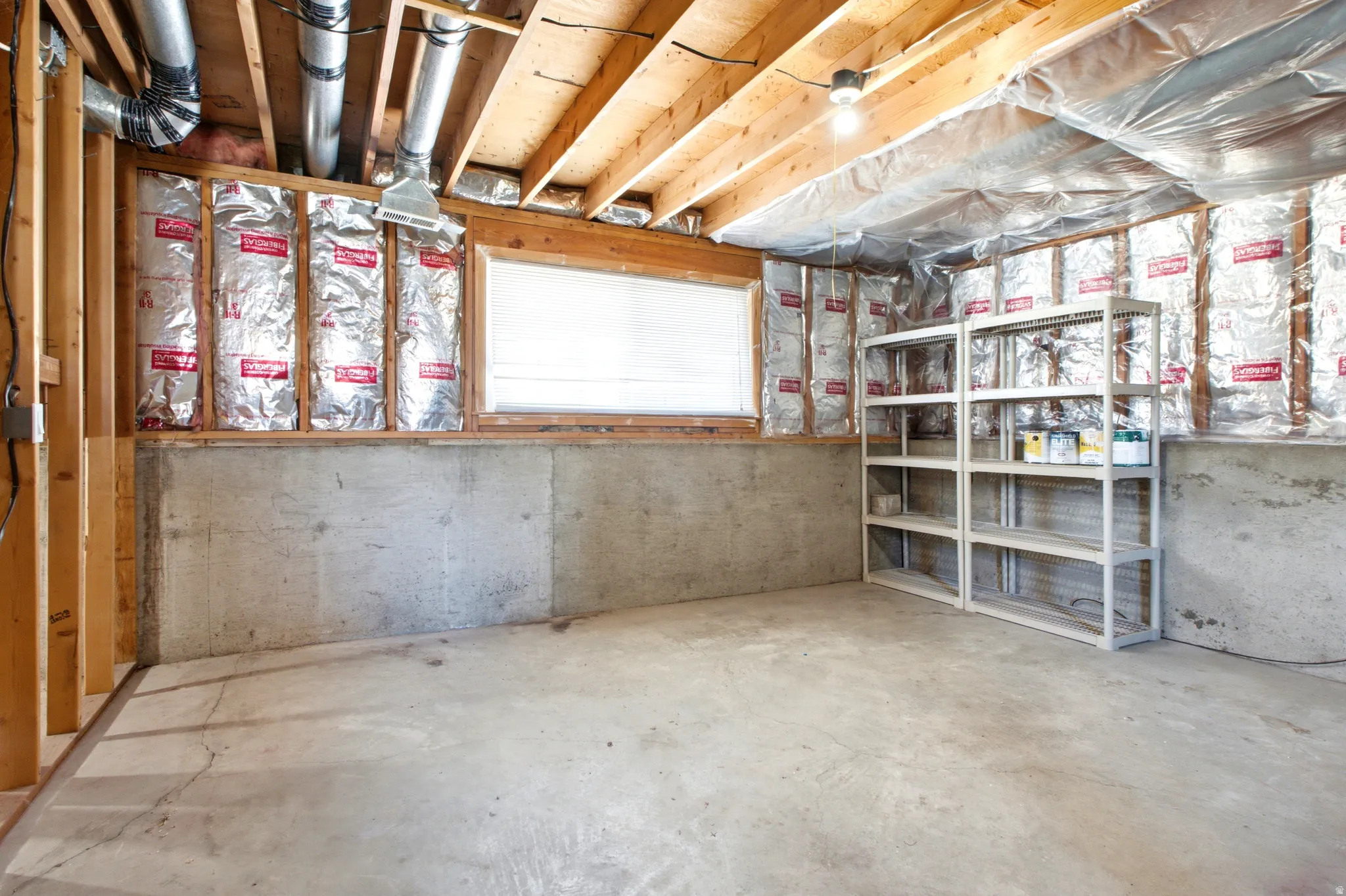 Unfinished basement space featuring exposed wooden ceiling joists, concrete flooring, and insulated framed walls