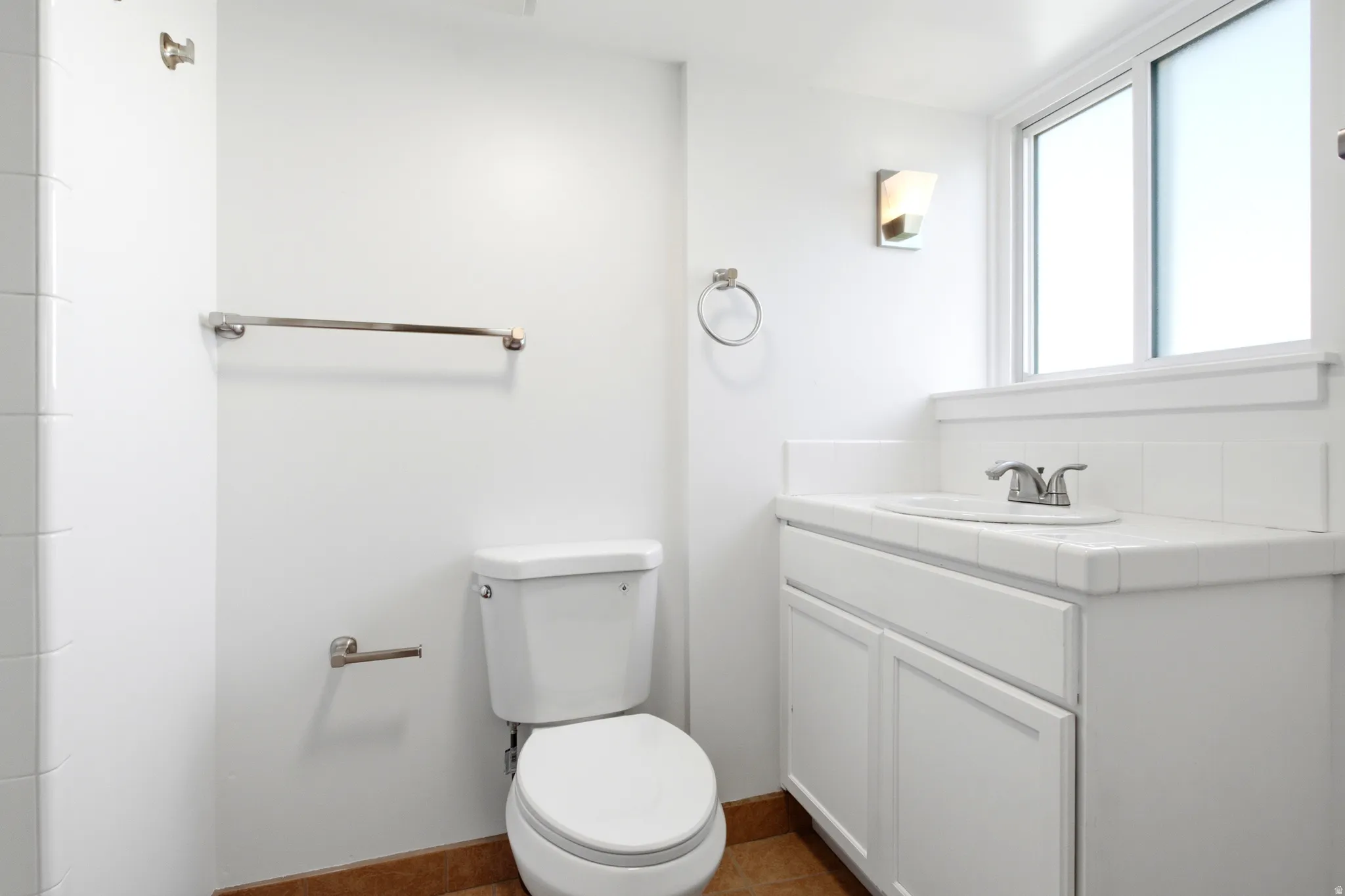 Bathroom featuring a white vanity with integrated sink, chrome fixtures, and a window with frosted privacy glass