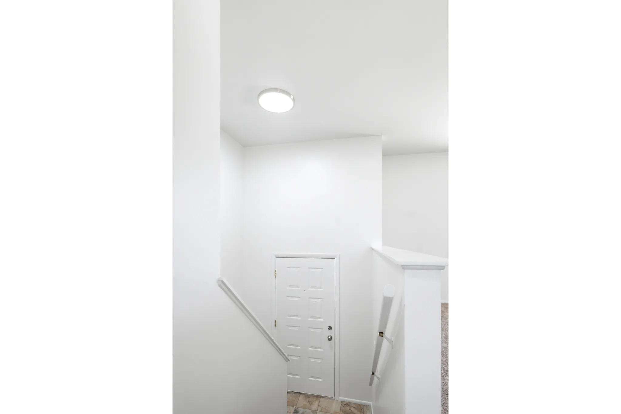 Stairwell featuring light-colored flooring, white walls, and a matching white door with a paneled design