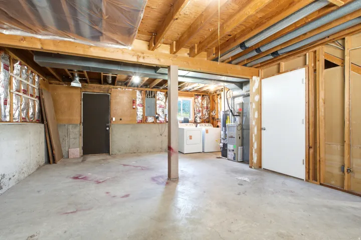 Unfinished basement featuring exposed wood beams, concrete flooring, and partial wall insulation