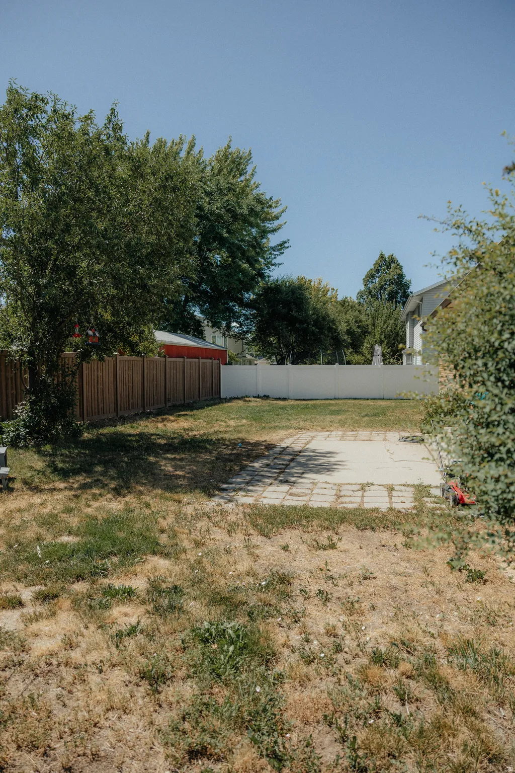 Expansive rear yard featuring a paved patio area, wood privacy fencing, and mature perimeter trees