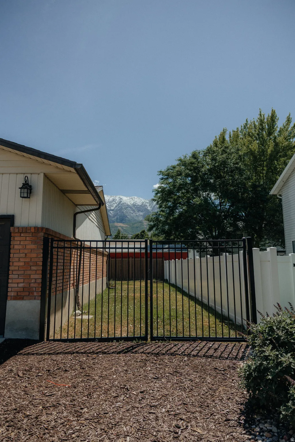 Gated side yard with a manicured lawn, brick facade, and a mountain backdrop