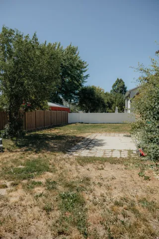 Expansive rear yard featuring a paved patio area, wood privacy fencing, and mature perimeter trees