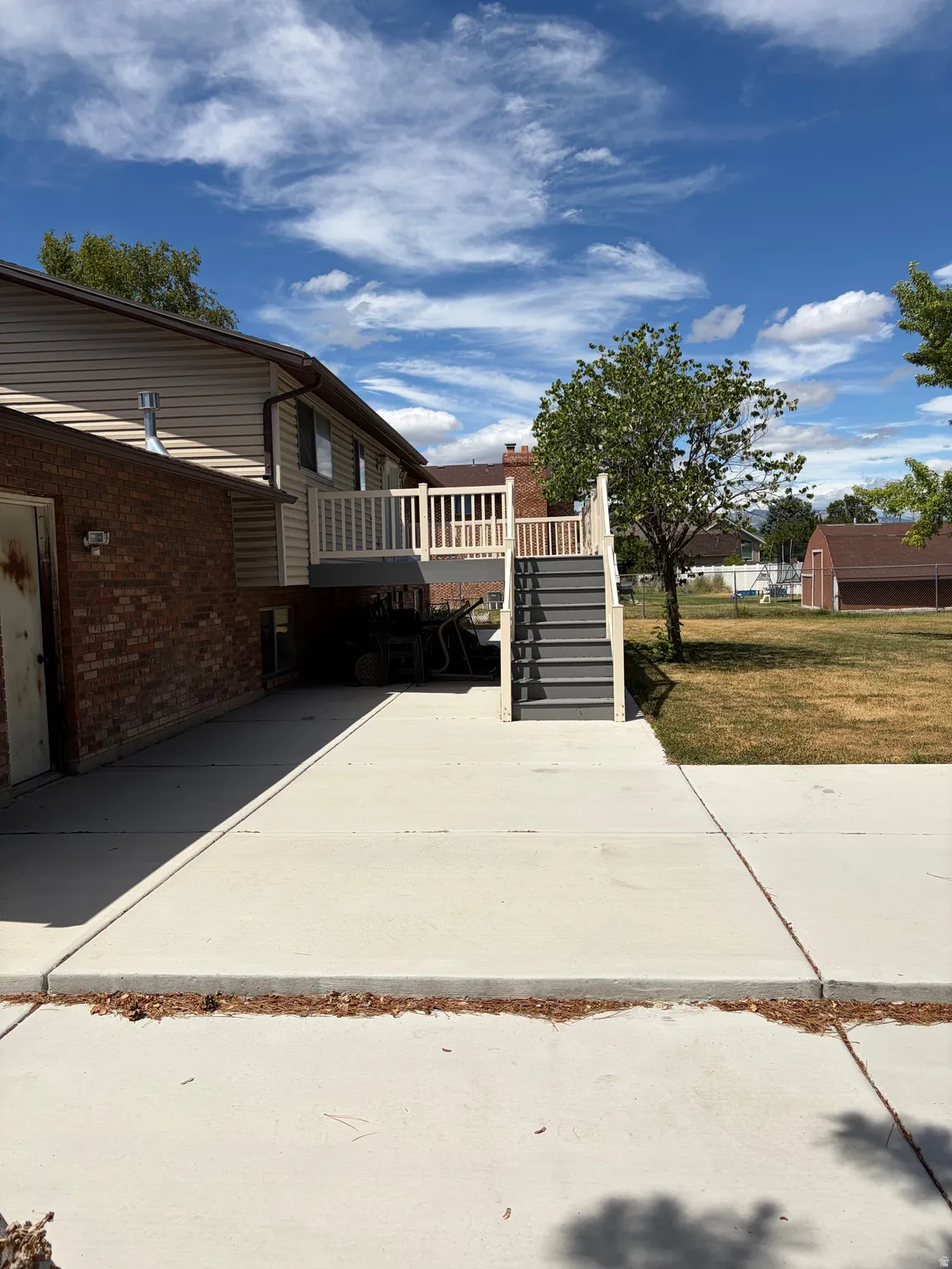 Rear exterior featuring a spacious concrete patio, multi-level deck with white railings, and a wide staircase