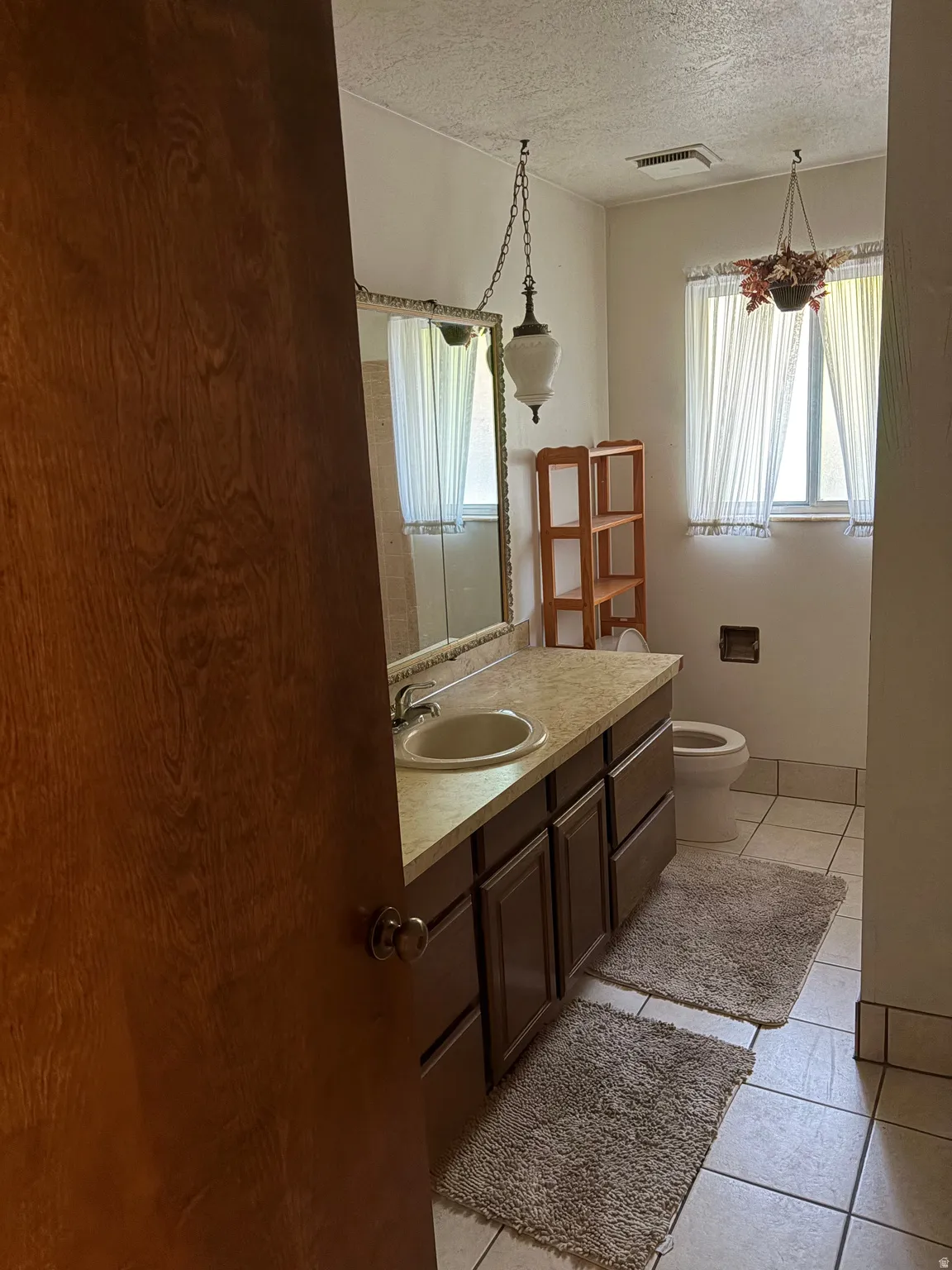 Bathroom featuring a wood-finish vanity with an integrated sink, a large wall-mounted mirror, and tile flooring