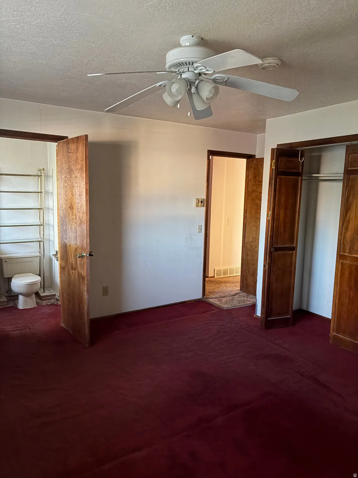 Ceiling fan with integrated lighting, wood-finish interior doors, built-in closet with bi-fold wood doors, wall-mounted towel rack, and a ceramic toilet fixture