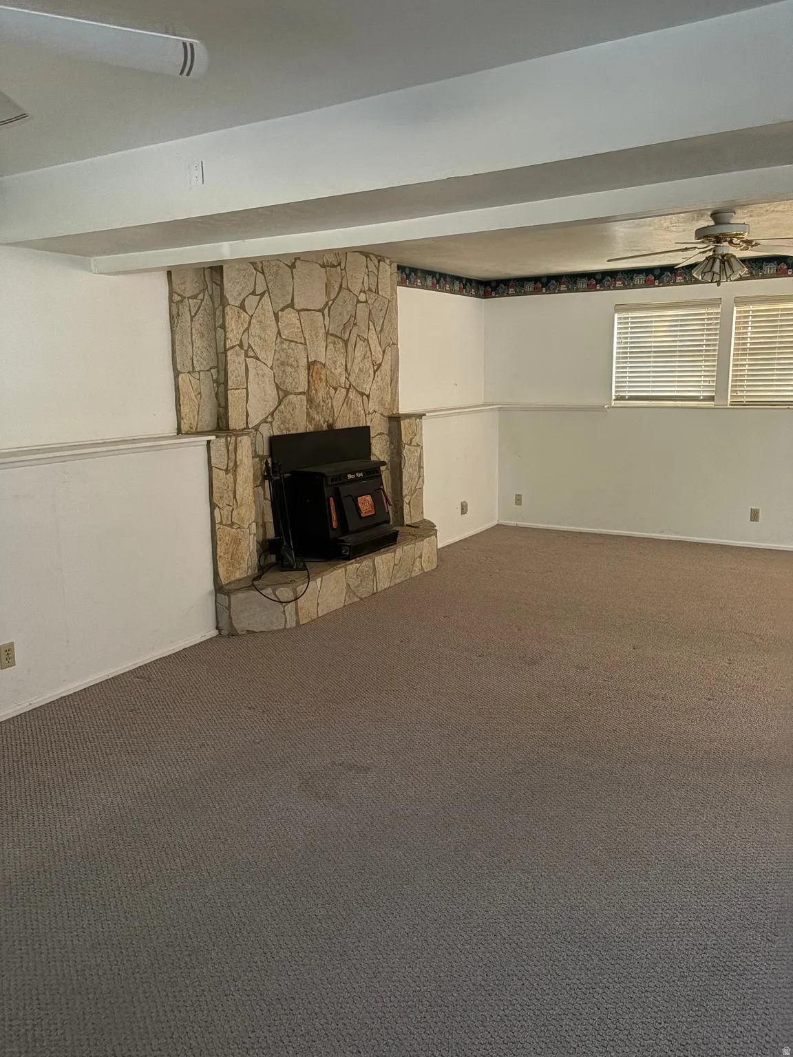 Stone-clad fireplace with a hearth, wood-burning stove, and ceiling fan