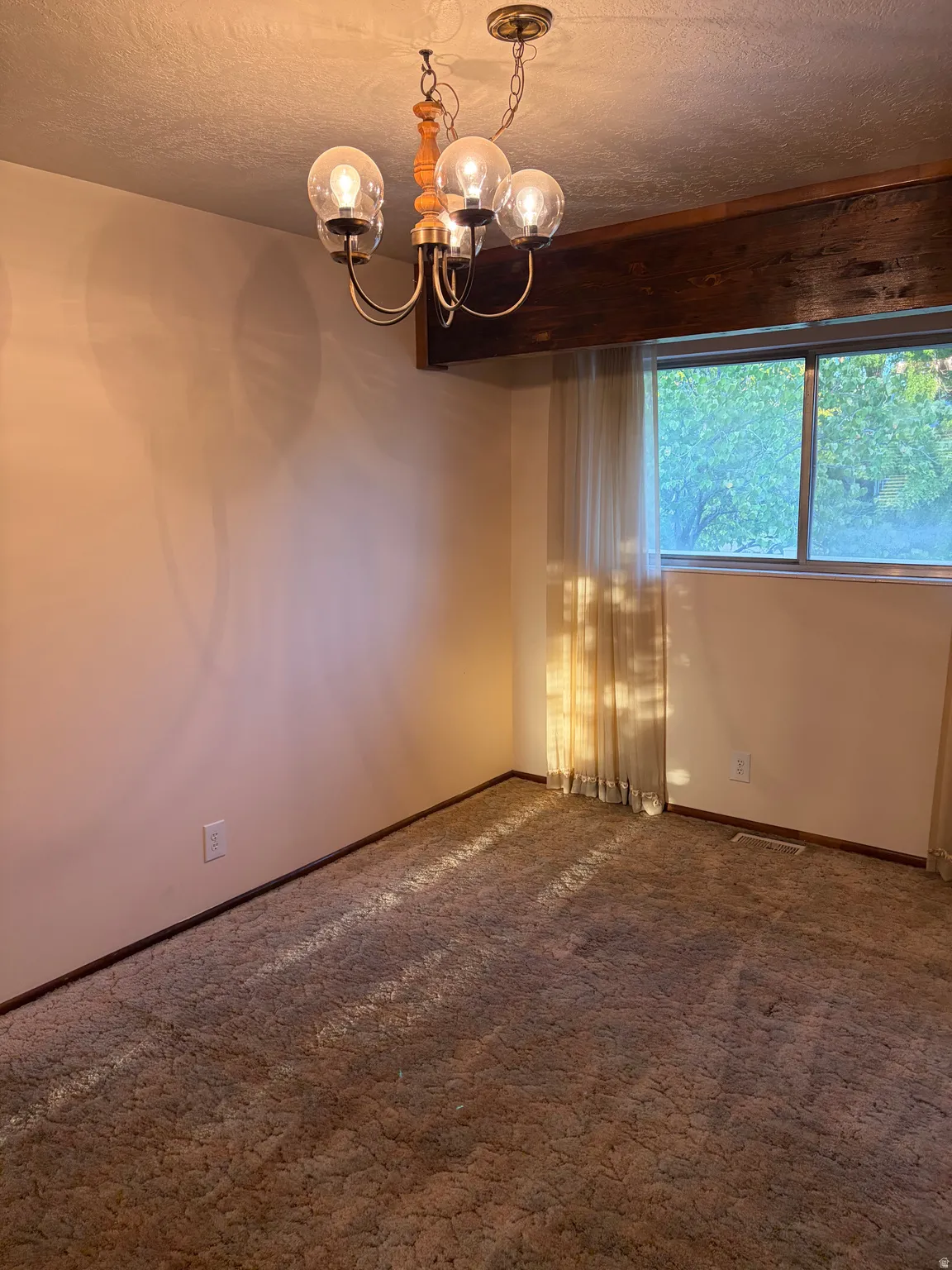 Recessed window with drapes, mounted light fixture, and wood ceiling beam
