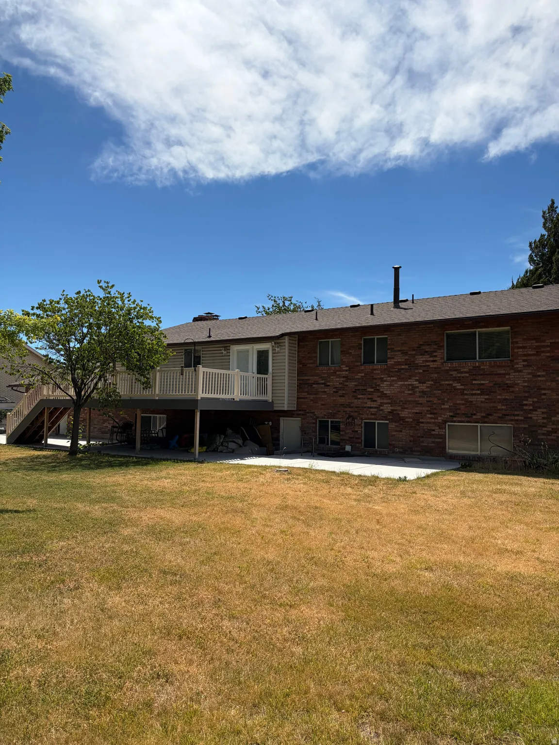 Spacious backyard featuring a multi-level deck, brick exterior, and a lower-level concrete patio