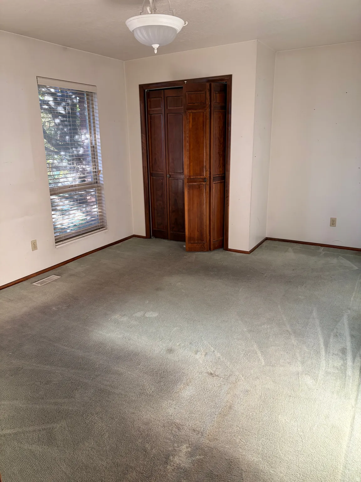 Recessed window with blinds, dark wood bi-fold closet doors, wall-to-wall carpeting, and a flush mount ceiling light fixture